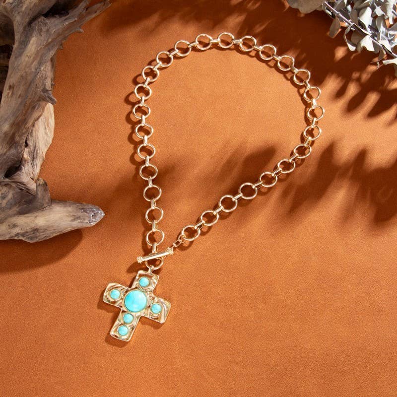 Gold chain bracelet with a turquoise cross pendant on an orange background