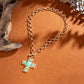 Gold chain bracelet with a turquoise cross pendant on an orange background